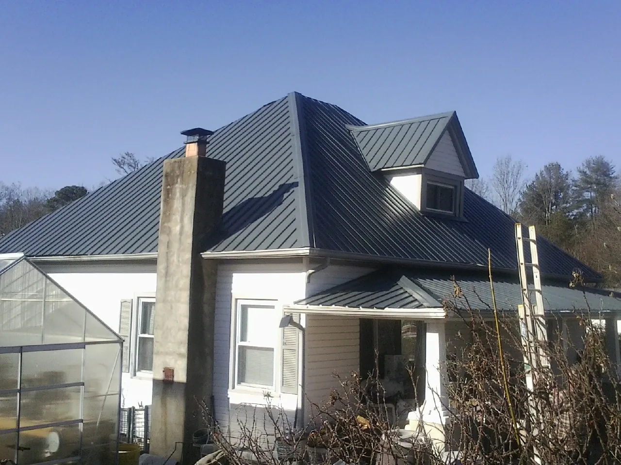 Dark blue standing seam metal roof on a white farmhouse with dormer — Slate & Tile Roof Repair by Roofing Brothers in Friendship