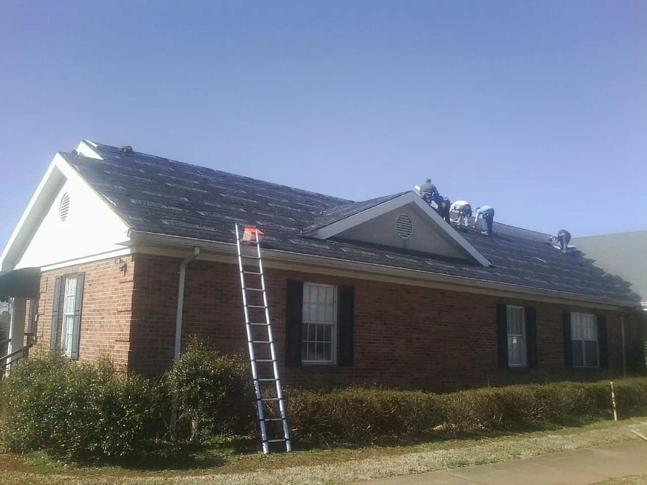 Crew tearing shingles off a brick ranch roof with a ladder set — Metal Roof Repair work by our crew in Friendship