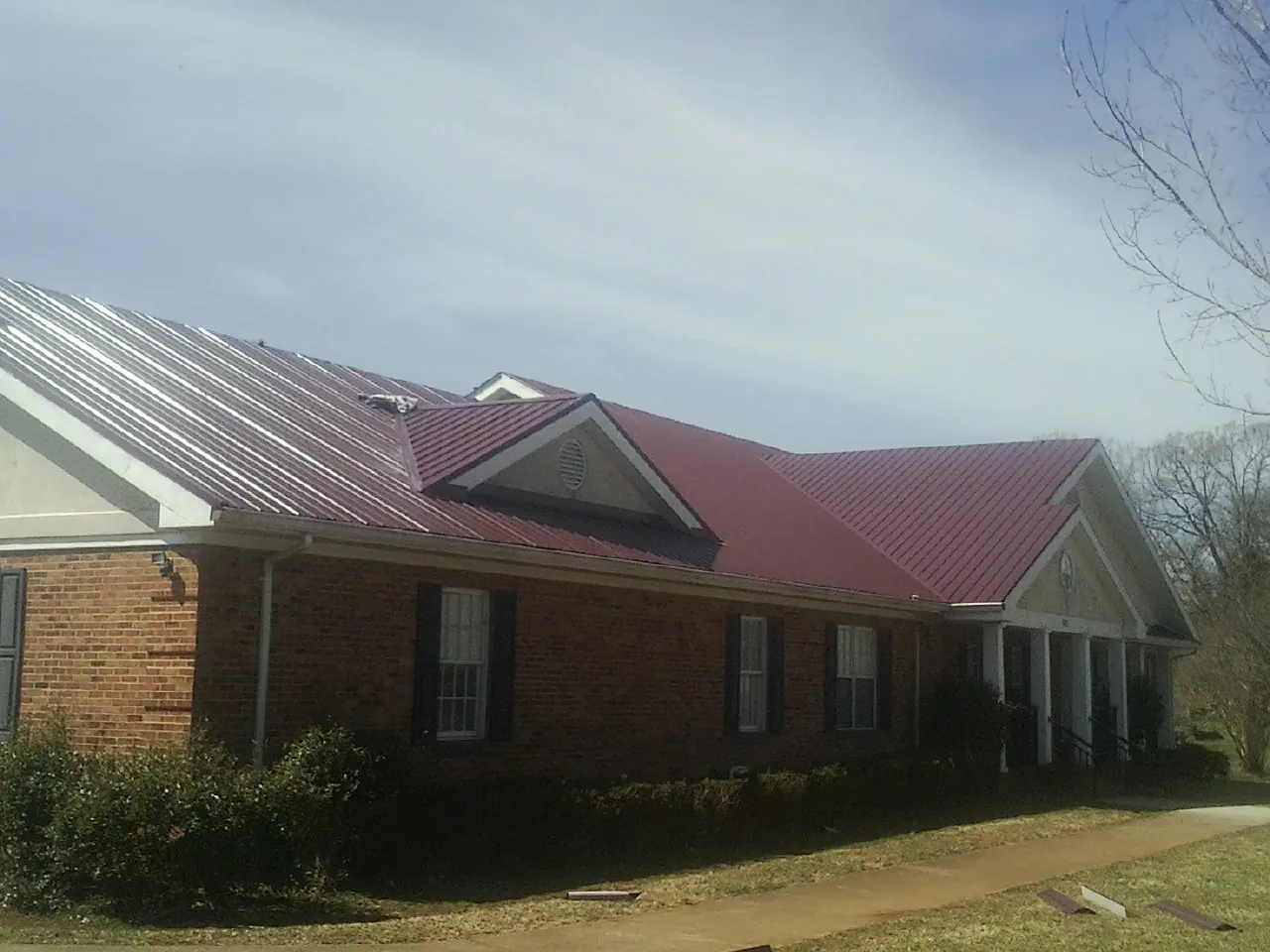 Red metal roof with gabled entries on a long brick building, from a Hail Damage Roof Repair job in Friendship