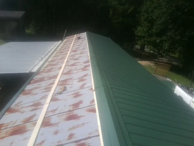 Old rusted panels beside newly installed green metal roofing — Wind Damage Roof Repair by Roofing Brothers in Friendship