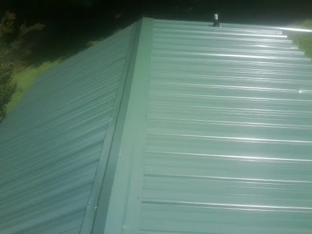 New green metal panels meeting at the ridge of a roof — Flat Roof Repair work by our crew in Friendship