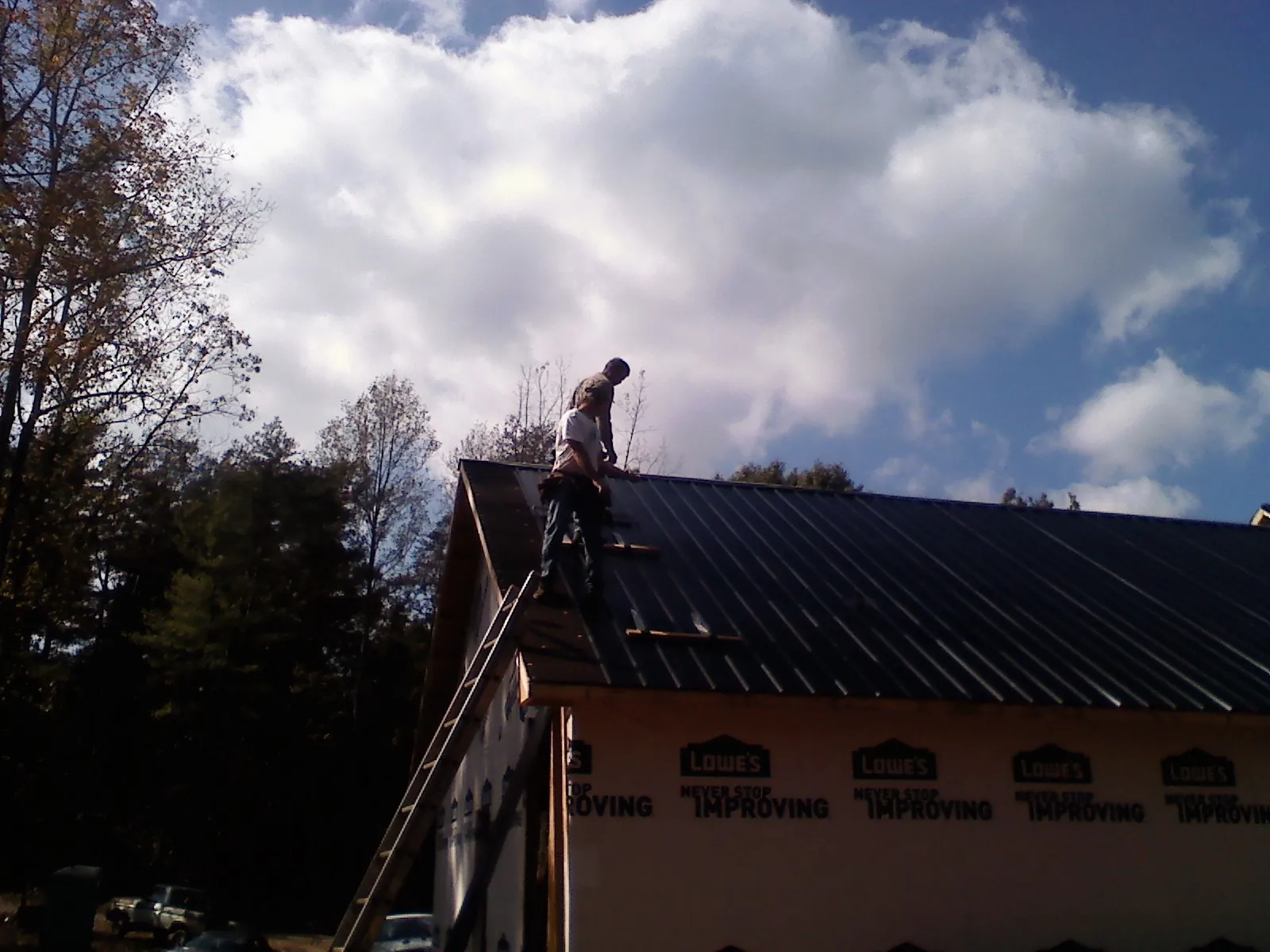 Roofer fastening dark metal panels high against a cloudy sky, from a Roof Inspection job in Friendship