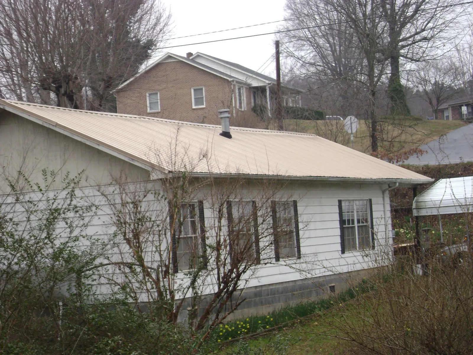 Tan metal roof on a white sided house set into a hillside — Commercial Roofing by Roofing Brothers in Friendship